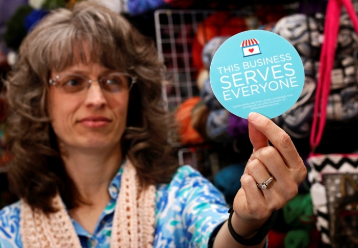 Elizabeth Ladd, owner of River Knits Fine Yarns, poses while holding up a 'This businesses serves everyone' sticker she plans to place outside her business in downtown Lafayette, Indiana, March 31, 2015. Indiana's Republican Governor Mike Pence, responding to national outrage over the state's new Religious Freedom Restoration Act, said on Tuesday he will 'fix' it to make clear businesses cannot use the law to deny services to same-sex couples.