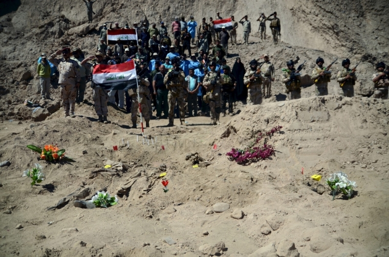 Iraqi soldiers salute as they stand next to a mass grave for Shiite soldiers from Camp Speicher who have been killed by Islamic State militants in the presidential compound of the former Iraqi president Saddam Hussein in Tikrit, April 6, 2015. Iraqi forensic teams began on Monday excavating 12 suspected mass grave sites thought to hold the corpses of as many as 1,700 soldiers massacred last summer by Islamic State militants as they swept across northern Iraq.