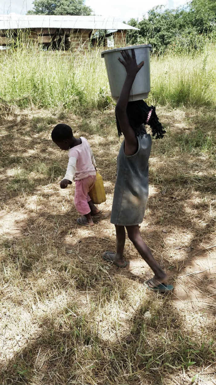 Two sisters, aged 6 and 3, carry containers of water March 24, 2015, in Bulanda, Zambia.