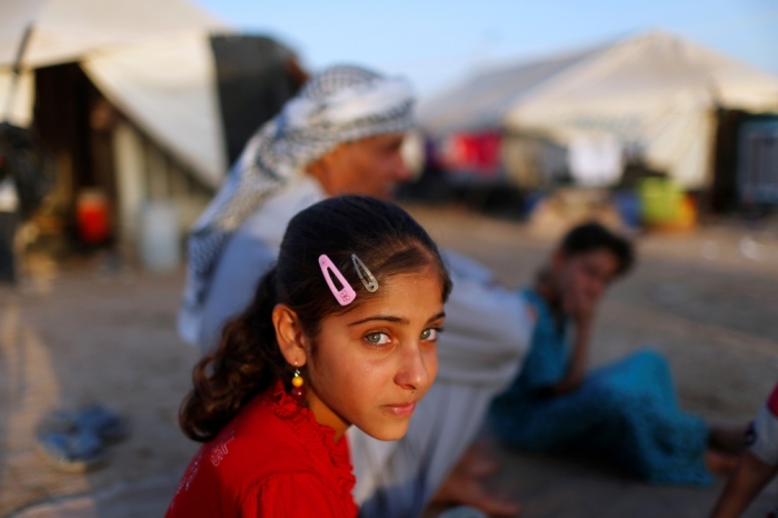 A displaced Iraqi child, who fled from Islamic State violence in Mosul, sits with her family outside their tent at Baherka refugee camp in Erbil, September 14, 2014.