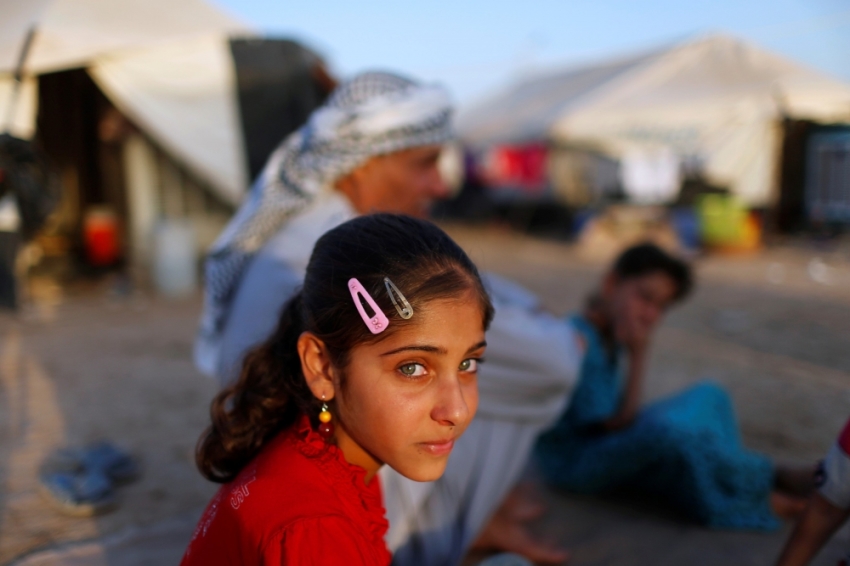 A displaced Iraqi child, who fled from Islamic State violence in Mosul, sits with her family outside their tent at Baherka refugee camp in Erbil, September 14, 2014.