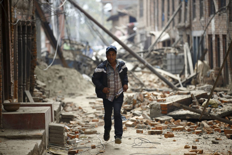 A man runs past damaged houses as aftershocks of an earthquake are felt a day after the earthquake in Bhaktapur, Nepal April 26, 2015. Rescuers dug with their bare hands and bodies piled up in Nepal on Sunday after the earthquake devastated the heavily crowded Kathmandu valley, killing at least 1,900, and triggered a deadly avalanche on Mount Everest.