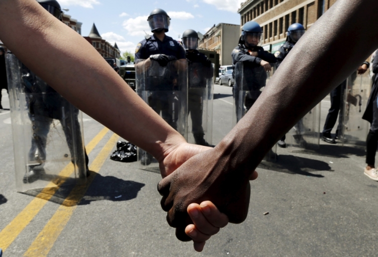Members of the community hold hands in front of police officers in riot gear outside a recently looted and burned CVS store in Baltimore, Maryland, April 28, 2015. The day after rioters tore through Baltimore, the city's mayor was criticized on Tuesday for a slow police response to some of the worst U.S. urban unrest in years after the funeral of Freddie Gray, a 25-year-old black man who died in police custody. Maryland Governor Larry Hogan said he had called Mayor Stephanie Rawlings-Blake repeatedly Monday but that she held off calling in the National Guard until three hours after violence first erupted.