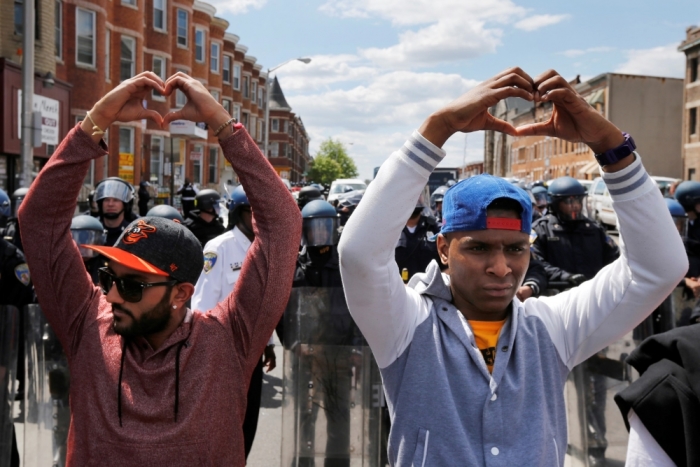 Members of the community make heart gestures with their hands in front of a line of police officers in riot gear, near a recently looted and burned CVS store in Baltimore, Md., on April 28, 2015.