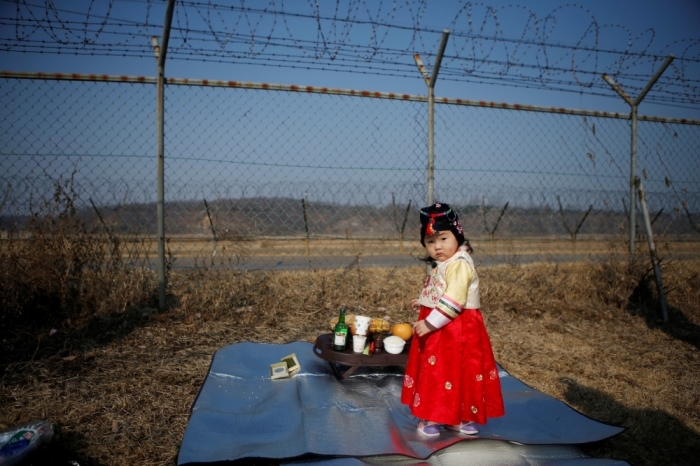 A girl dressed in a Hanbok, a Korean traditional costume, stands in front of a barbed-wire fence, as her parents prepare for a memorial service for North Korean family members, near the demilitarized zone separating the two Koreas, in Paju, February 19, 2015, on the occasion of Seolnal, the Korean Lunar New Year's day. Millions of South Koreans traveled to their hometowns during the three-day holiday which started last Wednesday. Seolnal is one of the traditional holidays when most Koreans visit their hometowns to be united with their families and hold memorial services for their deceased ancestors.