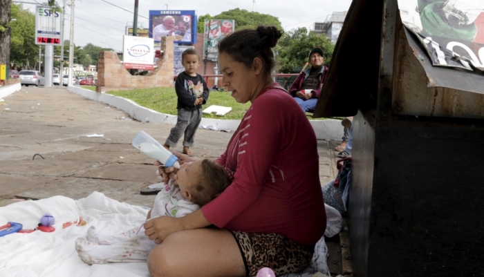 A woman living in poverty gives milk to her baby near a poster of Pope Francis (top), in Asuncion, May 8, 2015. The Pope will celebrate two masses, visit a children's hospital and poor neighborhoods along the Paraguay River wetlands during his visit.