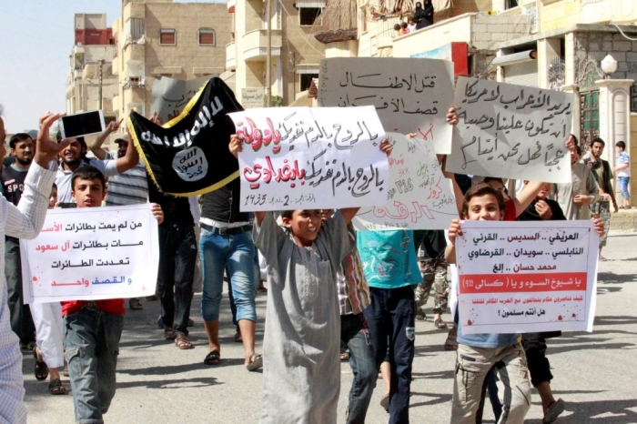 Youths carry banners during a protest against the U.S. airstrikes on the Islamic State (IS) in Raqqa September 26, 2014. The banners in Arabic read, 'By the soul, by the blood, we sacrifice ourselves oh state. by the soul, by the blood, we sacrifice ourselves oh Baghdadi' (C),'Who did not die by Assad's planes, died by Saudi family planes, The planes became many, but the strikes are one' (L).