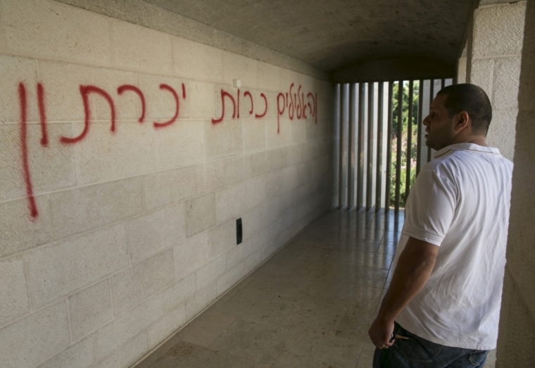 A man looks at graffiti that reads in Hebrew 'banish false gods' spray-painted on a wall in the Church of Loaves and Fishes on the shores of the Sea of Galilee in northern Israel, June 18, 2015. An arson attack on Thursday gutted part of the church at the site where Christians believe Jesus performed a miracle by feeding 5,000 people with five loaves of bread and two fish on the shore of the Sea of Galilee, the Israeli fire brigade said. A verse from a Hebrew prayer denouncing the worship of 'false gods' was spraypainted in red on a church wall, suggesting Jewish zealots were responsible.