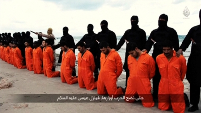 Men in orange jumpsuits purported to be Egyptian Christians held captive by the Islamic State kneel in front of armed men along a beach said to be near Tripoli, in this still image from an undated video made available on social media on February 15, 2015.<br>