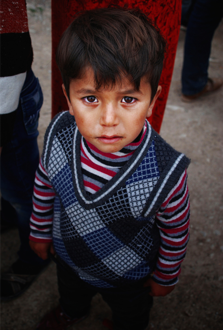 A young refugee waits for his parents as they collect food rations in Northern Iraq, March 2015.