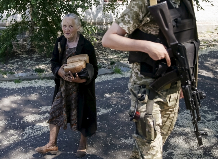 A local resident carries bread as a Ukrainian serviceman stands guard in the village of Novotoshkivske near the frontline with pro-Russian separatists, eastern Ukraine, June 8, 2015.