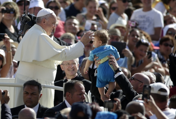 Pope Francis blesses a baby as he arrives to lead his weekly audience in Saint Peter's Square at the Vatican, August 27, 2014.