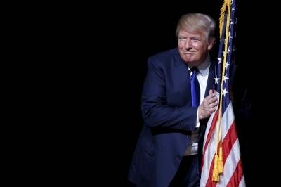 Donald Trump hugs a U.S. flag as he takes the stage for a campaign town hall meeting in Derry, New Hampshire August 19, 2015.
