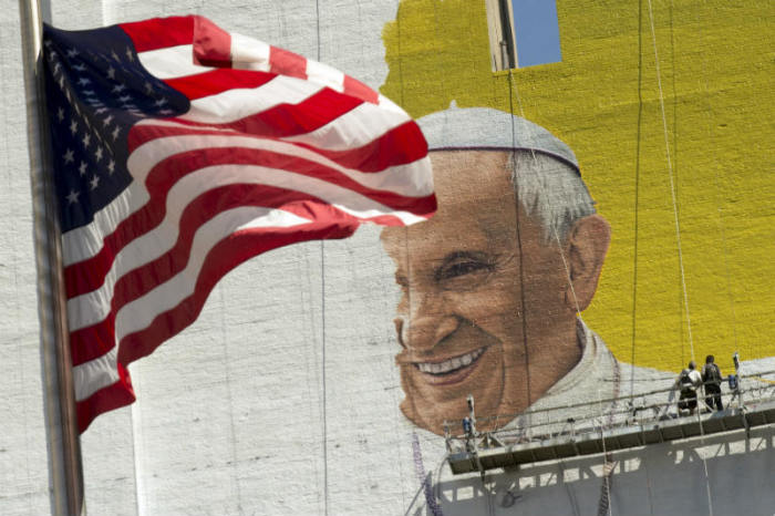 The U.S. flag flies as painters work on a mural of Pope Francis on the side of a building in midtown Manhattan in New York City Aug. 28, 2015. Pope Francis is scheduled to visit Washington D.C., New York and Philadelphia Sept. 22-27.