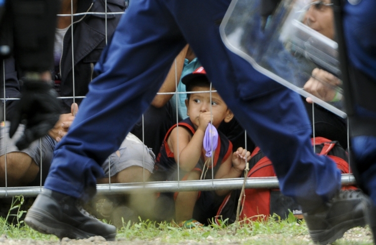 A boy sits behind a fence as a police officer walks past at the migrant reception centre in Roszke, Hungary, September 4, 2015. Some 300 migrants broke out of a Hungarian border camp on Friday and hundreds of others set off on foot from Budapest as police scrambled to keep control of a migrant crisis that has brought Europe's asylum system to breaking point.