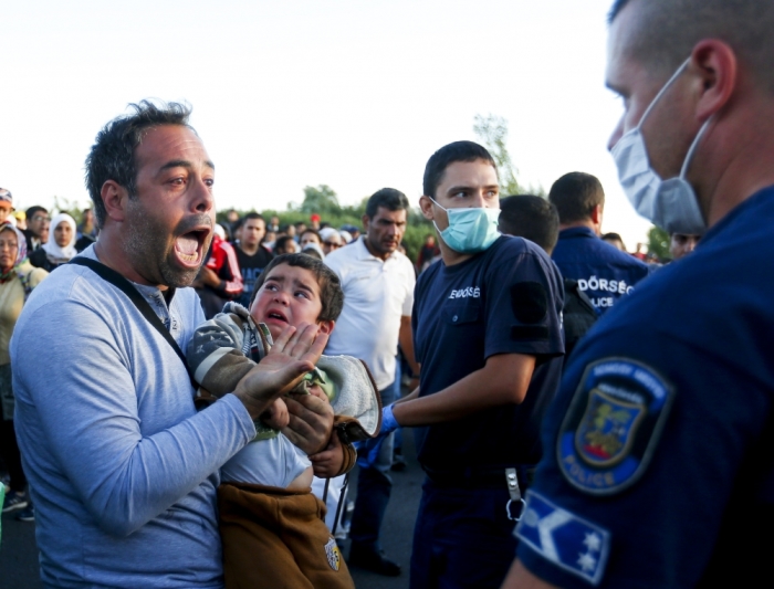An exhausted migrant holds his son as he speaks to a police officer at a collection point in the village of Roszke, Hungary, September 7, 2015.