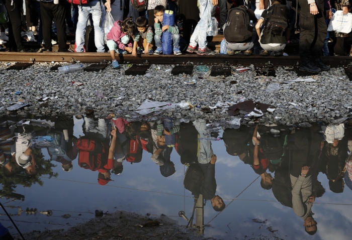 Syrian refugees are reflected in a puddle as they wait for their turn to enter Macedonia at Greece's border, near the Greek village of Idomeni, September 11, 2015. Some 7,600 migrants, many of them refugees from the Syrian war, entered Macedonia from Greece between 6 p.m. (1600 GMT) on Wednesday and 6 p.m. on Thursday, an official with the United Nations refugee agency said on the border.