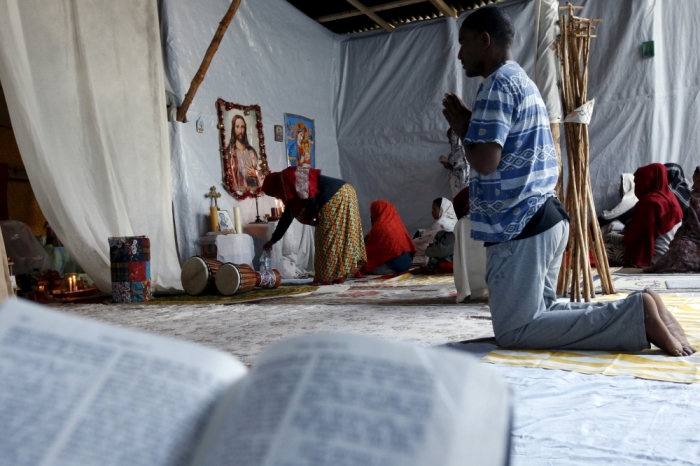 Christian migrants from Eritrea and Ethiopia pary and read the bible before Sunday mass at the makeshift church in 'The New Jungle' near Calais, France, August 2, 2015. Some 3,000 migrants live around the tunnel entrance in a makeshift camp known as 'The Jungle', making the northern French port one of the frontlines in Europe's wider migrant crisis. REUTERS/Pascal Rossignol