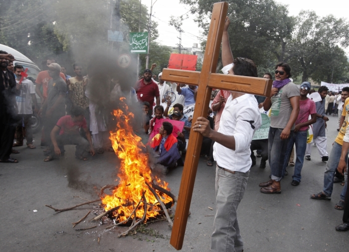 A member of the Pakistani Christian community holds a cross as he chants slogans in front of a fire during a protest rally to condemn Sunday's suicide attack in Peshawar on a church, with others in Lahore September 23, 2013. 