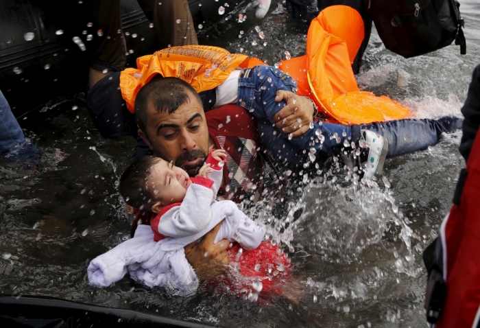 A Syrian refugee holds onto his children as he struggles to walk off a dinghy on the Greek island of Lesbos after crossing a part of the Aegean Sea from Turkey to Lesbos, Greece, September 24, 2015.