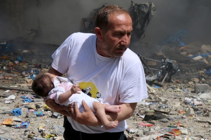 A man holds a baby that survived what activists said was a site hit by a barrel bomb dropped by forces loyal to Syrian President Bashar al-Assad at the old city of Aleppo, Syria, June 3, 2015.
