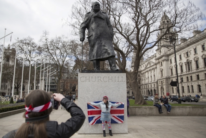 A woman is photographed by her companion as she poses with a Union Jack flag under a statue of former British Prime Minister Winston Churchill in London, England, March 22, 2015.