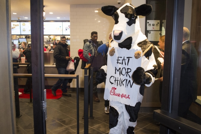 A Chick-fil-A mascot holds a sign as customers enter a Chick-fil-A freestanding franchise restaurant during its grand opening in Midtown, New York, October 3, 2015.