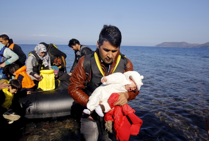 An Afghan migrant carries his one-month-old child as he disembarks from an overcrowded raft at a beach on the Greek island of Lesbos, October 19, 2015. 