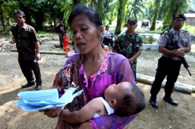 A resident holds her baby as she prays during attend Sunday mass as a soldier and policemen stand guard near a burned church at Suka Makmur Village in Aceh Singkil, Indonesia Aceh province, October 18, 2015. Hardline Muslims in Indonesia's conservative Aceh province on Sunday demanded the local government close 10 Christian churches, just days after a mob burnt down a church, leaving one person dead and several injured.