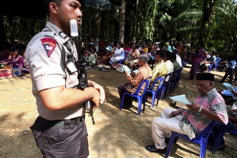 An Indonesian policeman holds a rifle as he guards residents during Sunday mass prayer beside a burned church at Suka Makmur Village in Aceh Singkil, Indonesia Aceh province, October 18, 2015. Hardline Muslims in Indonesia's conservative Aceh province on Sunday demanded the local government close 10 Christian churches, just days after a mob burnt down a church, leaving one person dead and several injured.