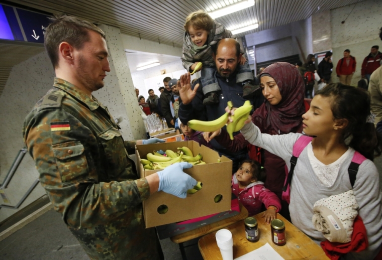 A German Bundeswehr, armed forces soldier distrubutes food to migrants before they are transported by bus to a refugee camp in the capital after arriving by train from Salzburg, Austria at Schoenefeld railway station in Berlin, Germany, October 5, 2015.