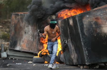 A Palestinian protester takes cover during clashes with Israeli troops near the Jewish settlement of Bet El, near the West Bank city of Ramallah, October 23, 2015. Palestinian factions called for mass rallies against Israel in the occupied West Bank and East Jerusalem in a "day of rage" on Friday, as world and regional powers pressed on with talks to try to end more than three weeks of bloodshed.