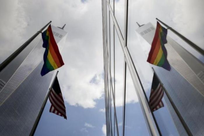 A gay pride flag flies alongside the U.S. flag (lower), as they are reflected off the front of 200 West Street, also known as the Goldman Sachs Tower, in lower Manhattan, New York June 26, 2015.