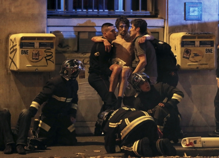 French fire brigade members aid an injured individual near the Bataclan concert hall following fatal shootings in Paris, France, November 13, 2015. At least 30 people were killed in attacks in Paris and a hostage situation was under way at a concert hall in the French capital, French media reported on Friday.
