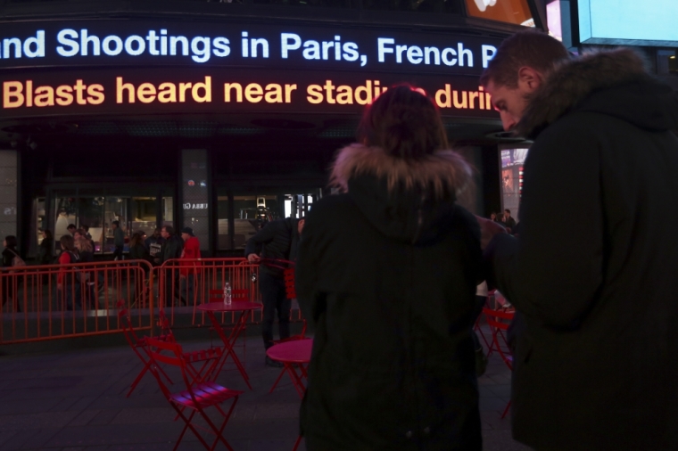 People watch as a news ticker displays news of the shooting attacks in Paris, in Times Square in the Manhattan borough of New York, November 13, 2015.