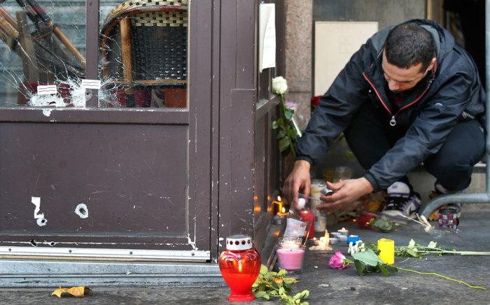 Bullet impacts are seen in cafe window as a man places a candle outside one of the attack sites in Paris, November 15, 2015.