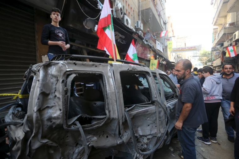 Residents inspect a burnt vehicle at the site of the two explosions that occurred on Thursday in the southern suburbs of the Lebanese capital Beirut, November 13, 2015.
