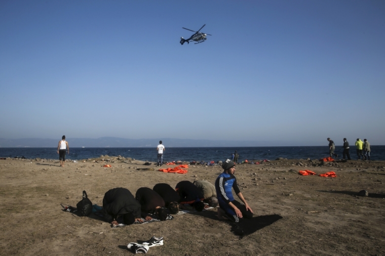 A Frontex helicopter flies over as Syrian refugees pray after arriving on a boat on the Greek island of Lesbos, November 6, 2015. Since the start of the year, over 590,000 people have crossed into Greece, the frontline of a massive westward population shift from war-ravaged Syria and beyond.