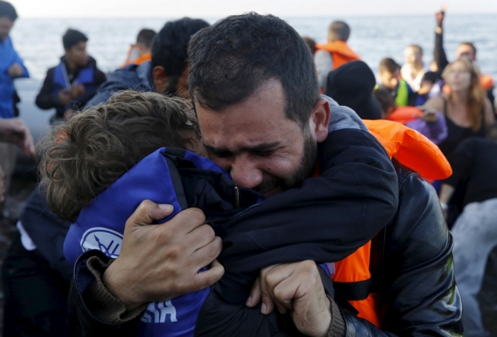 A Syrian refugee embraces his son after their overcrowded raft landed at a rocky beach in the Greek island of Lesbos, November 19, 2015.