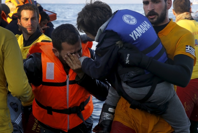 A Syrian refugee kisses the hand of his son held by a Greek life guard after their overcrowded raft landed at a rocky beach in the Greek island of Lesbos, November 19, 2015. Balkan countries have begun filtering the flow of migrants to Europe, granting passage to those fleeing conflict in the Middle East and Afghanistan but turning back others from Africa and Asia, the United Nations and Reuters witnesses said on Thursday.