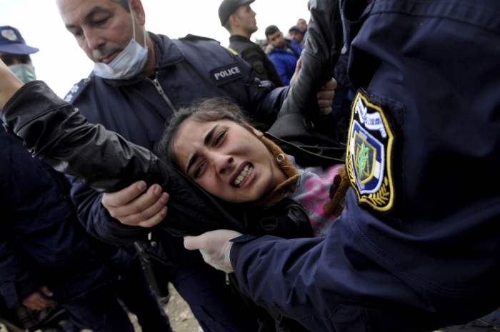 Greek policemen carry away a woman as Syrian, Iraqi and Afghan refugees who try to force their way through the Greek-Macedonian borders are pushed back by Greek police, near the village of Idomeni, Greece November 22, 2015.
