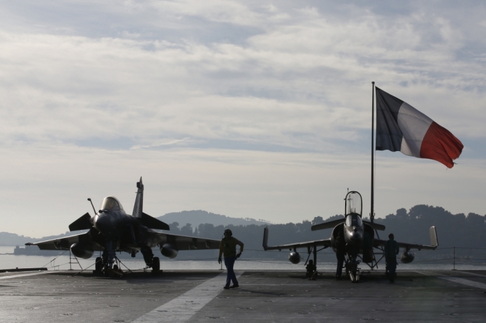 Flight deck crew work around a Rafale (L) and a Super Etendard fighter jets as a French flag flies aboard the French nuclear-powered aircraft carrier Charles de Gaulle before its departure from the naval base of Toulon, France, November 18, 2015. France's Charles de Gaulle aircraft carrier will be deployed today to support operations against Islamic State in Syria and Iraq.