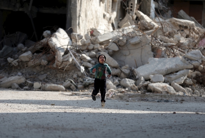 A boy runs in front of damaged buildings in the Douma neighborhood of Damascus, Syria, November 26, 2015.