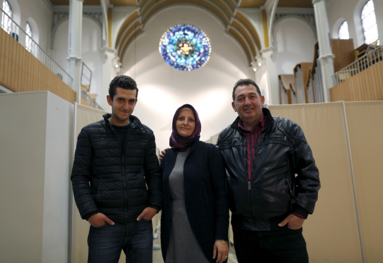 Members of a migrant Syrian family, Zabyl Olabi (C), her husband Mahmod and their 18-year-old son Humam (L), who came from Haleb near Aleppo, pose inside a Protestant church in Oberhausen, Germany November 19, 2015. Up to 140 refugees are landing in Oberhausen every week, forcing authorities to come up with new locations to house them. City officials say they had little choice but to use the church. In early November, workers removed the altar and dozens of chairs, replacing them with metal beds, which are separated by makeshift partitions to give the church's new residents a semblance of privacy.