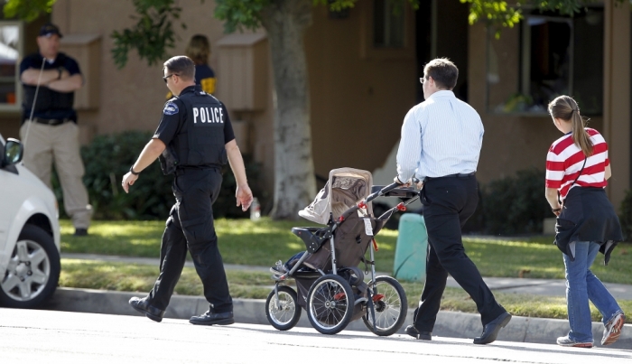Residents are escorted by a police officer as they walk by the residence that is in connection to the shootings in San Bernardino, California, December 3, 2015. Authorities on Thursday were working to determine why a man and a woman opened fire at a holiday party of his co-workers in Southern California, killing 14 people and wounding 17 in an attack that appeared to have been planned.
