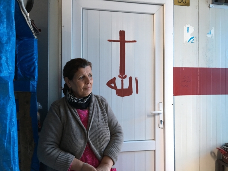 An Iraqi woman stands next to a door with a painted cross.