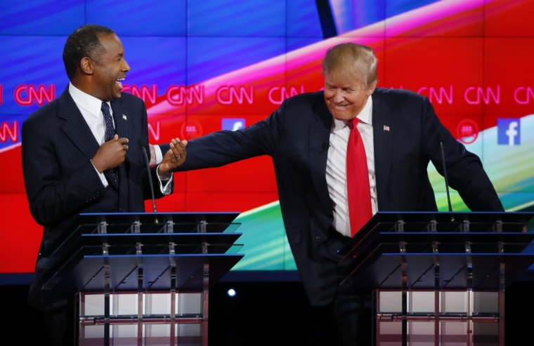 Republican U.S. presidential candidate businessman Donald Trump (R) reacts to a comment from Dr. Ben Carson (L) and reaches over to him in the midst of the Republican presidential debate in Las Vegas, Nevada December 15, 2015.
