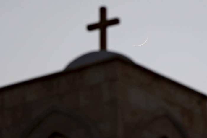 A cross on a Lutheran Church is pictured with the moon in the background during a celebration of the lighting of a 12-metre-tall Christmas tree in Shouneh, Jordan, December 13, 2015.