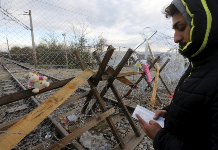 A stranded Iranian Christian migrant holds the Bible as he prays at dawn in front of a fence reinforced by barbed wire and a wooden barricade at the Greek-Macedonian border near to the Greek village of Idomeni, November 30, 2015. About 1,500 migrants mainly from Iran, Pakistan, Bangladesh, Morocco, Algeria, Somalia and other African and Asian countries have been stranded at the Greek-Macedonian border for nearly two weeks.