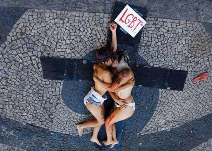 Two female feminist activists kiss on top of a cut-out cross in front of a church in Rio De Janeiro, Brazil in January of 2014.